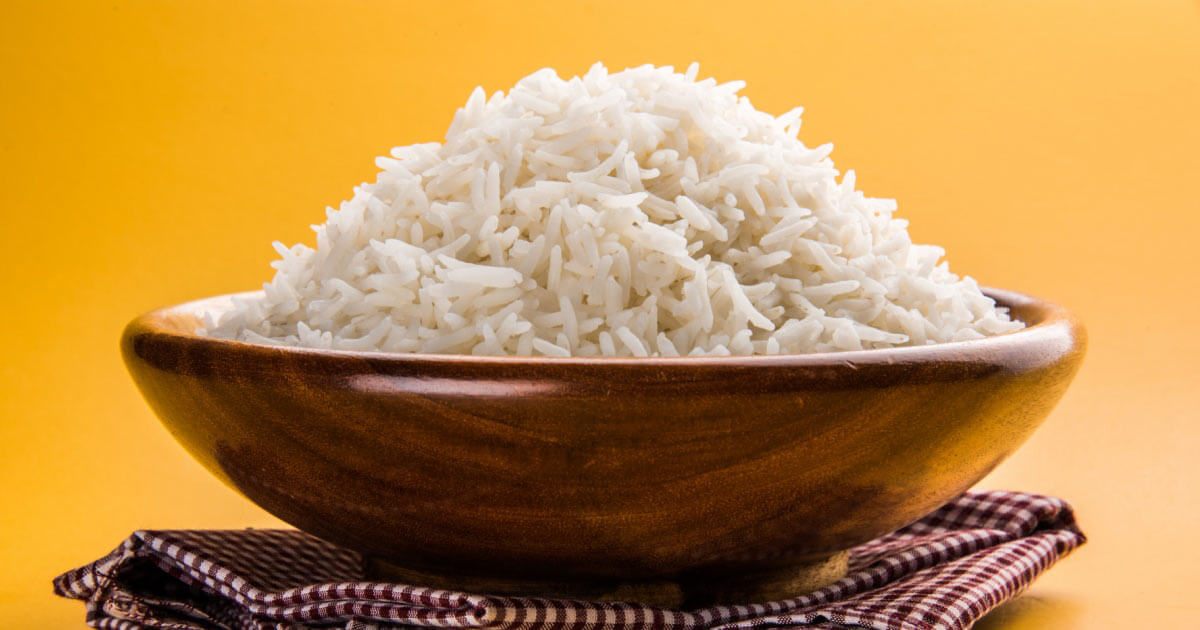 Gekochter Basmati-Reis, serviert in einer Holzschale mit gelbem Hintergrund.