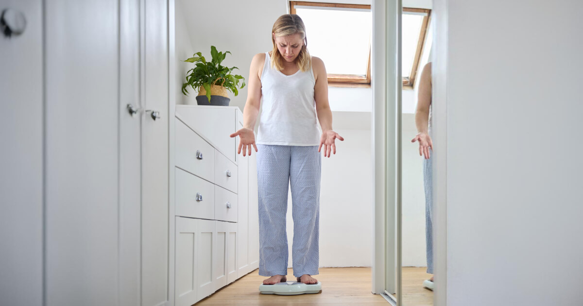 A woman standing on the scales looking frustratedly at the number.