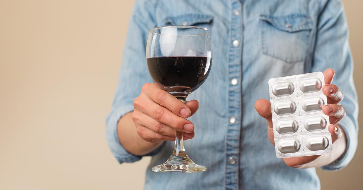 eine Frau hält ein Glas Rotwein in der rechten Hand und Antibiotika in der linken Hand