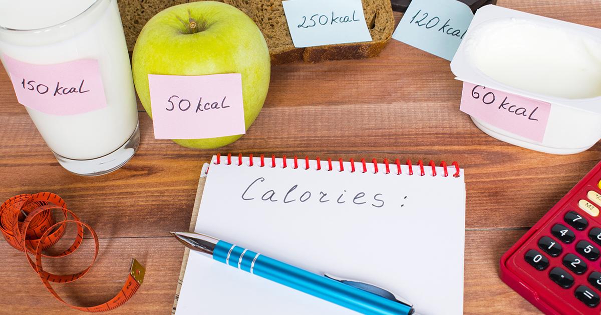 Forskellige fødevarer mærket med deres kalorieindhold ved siden af en notesbog og målebånd.