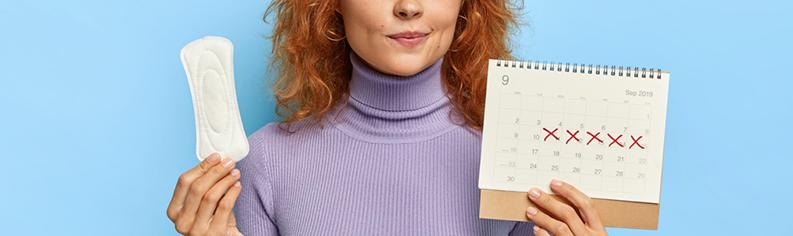 Ung kvinde med en kalender i den ene hånd og menstruationsbind i den anden hånd