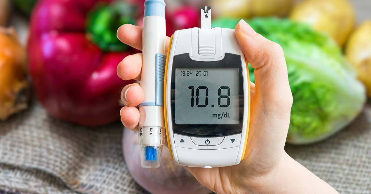 Person holding diabetes monitor in front of fruit and vegetables.