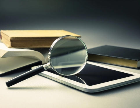 A magnifying glass on a smart tablet with some books
