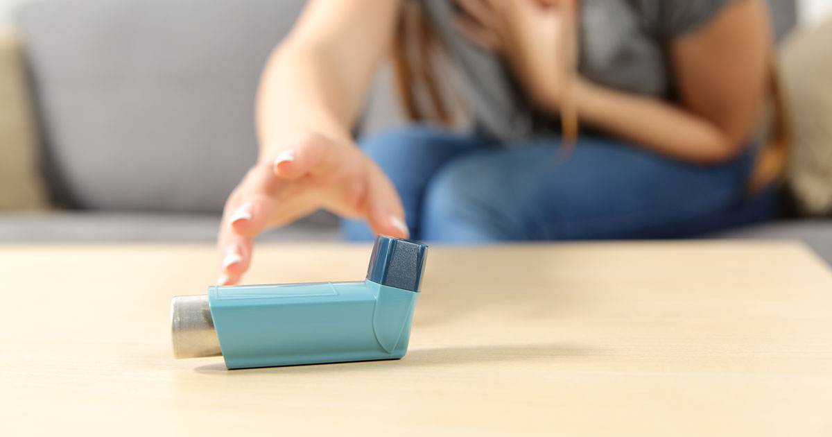 Woman reaching for blue asthma inhaler during an asthma attack.