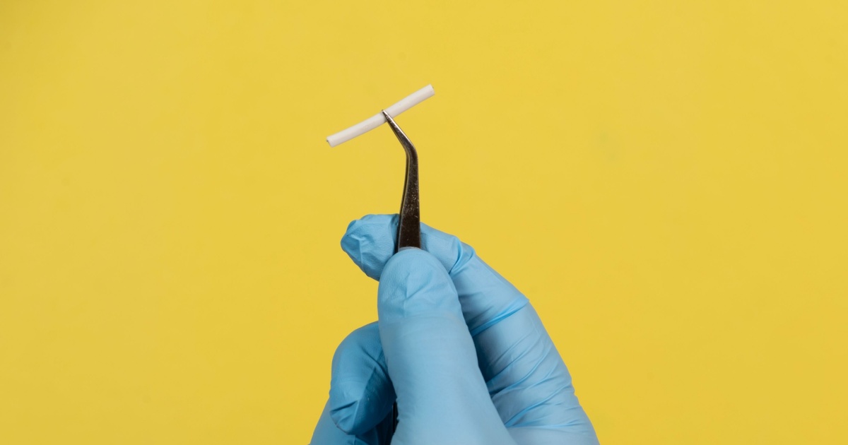A doctor holding the contraceptive implant with a pair of medical tweezers