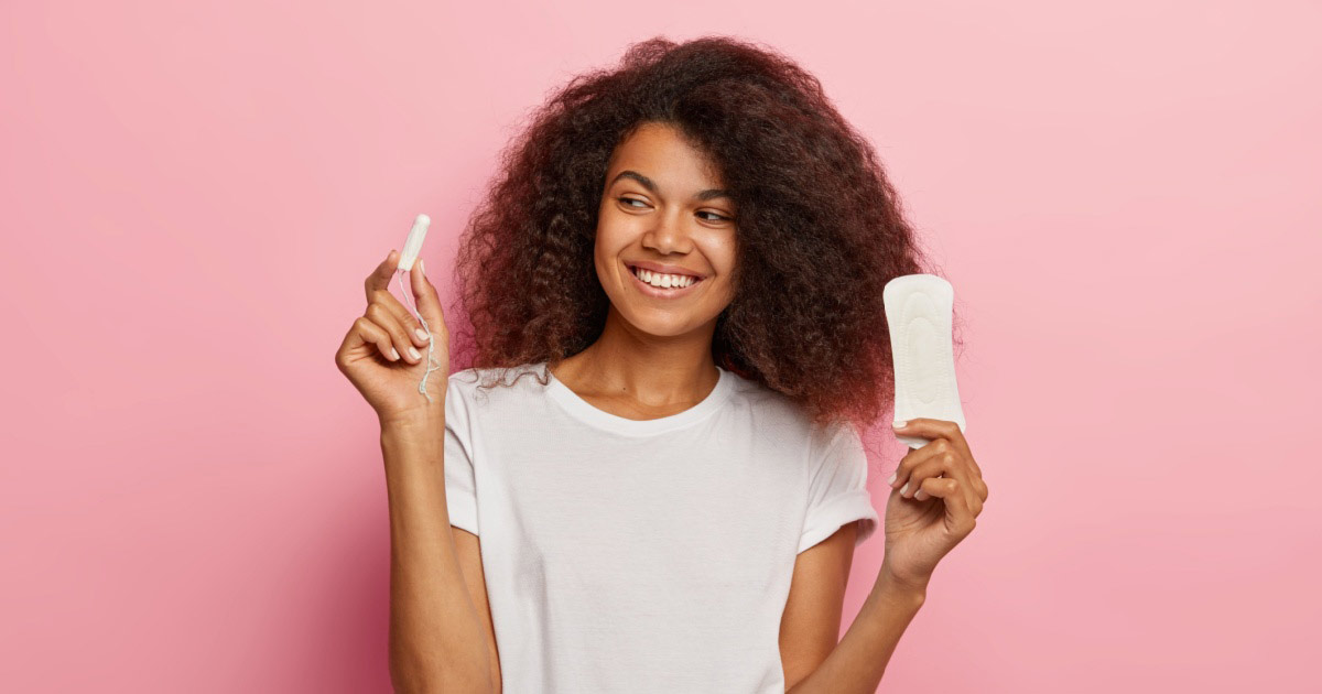 A woman smiling with a pink background, holding sanitary products.