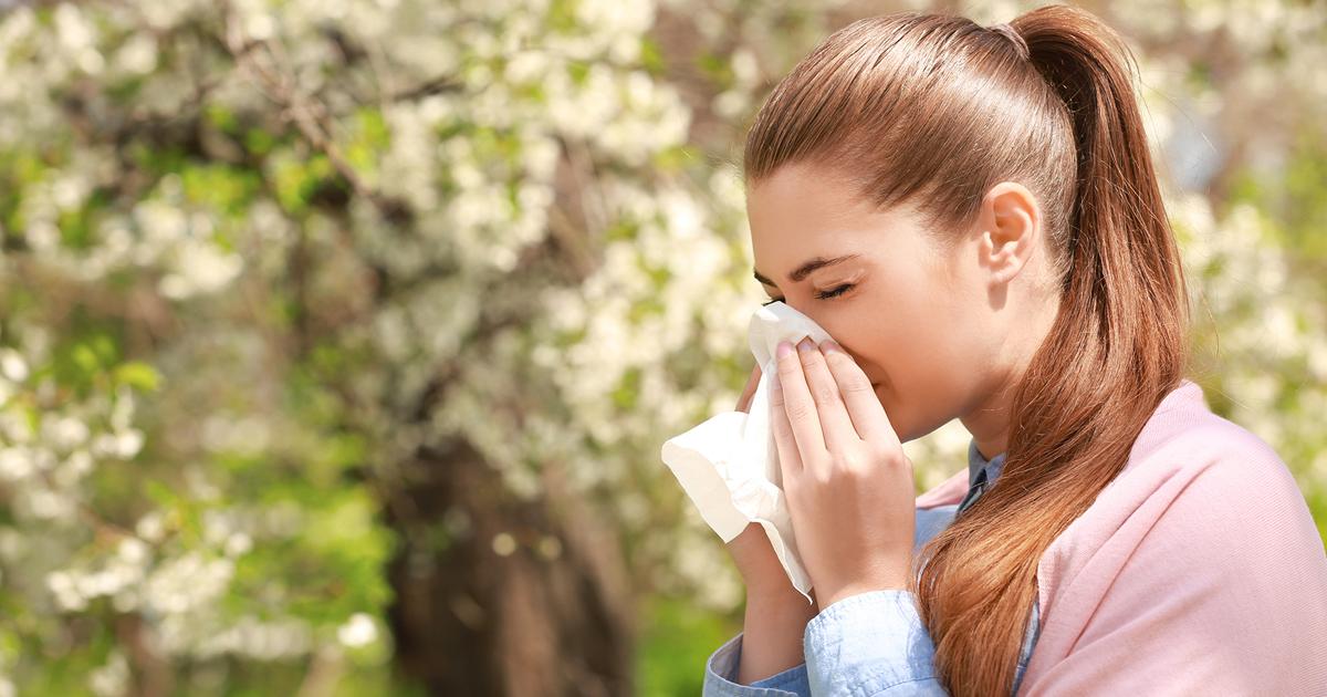 Young woman sneezes into tissue outside in spring.
