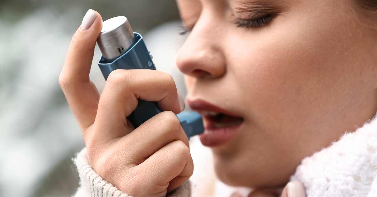 Inhalaattoria käyttävä nuori nainen, joka kärsii astmakohtauksesta.