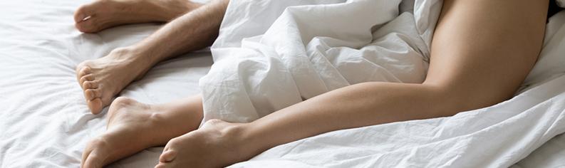 Un couple allongé sur un lit sous des draps blancs