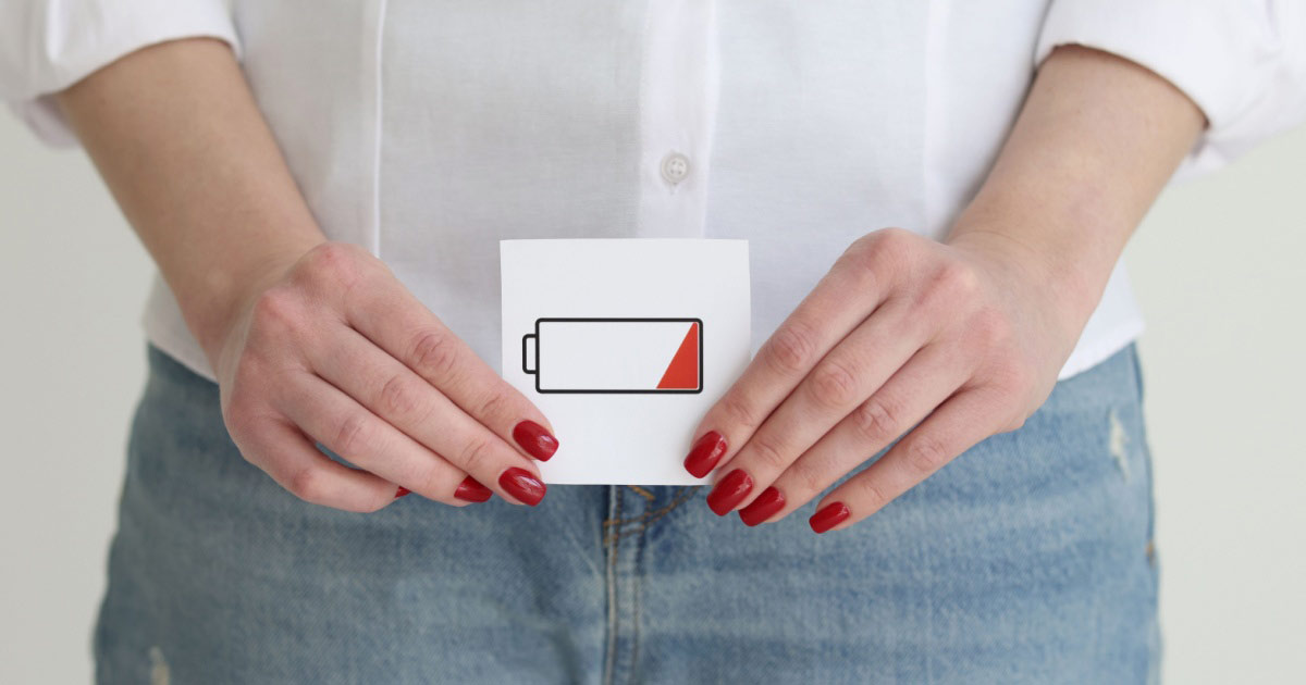 Une femme tenant un signe de batterie faible au-dessus de son entrejambe, suggérant une faible libido. 