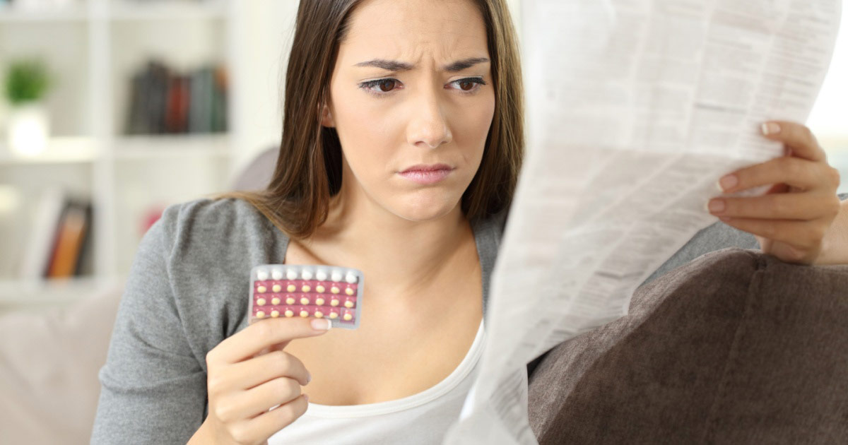 Jeune femme inquiète lisant la notice d'une pilule contraceptive.