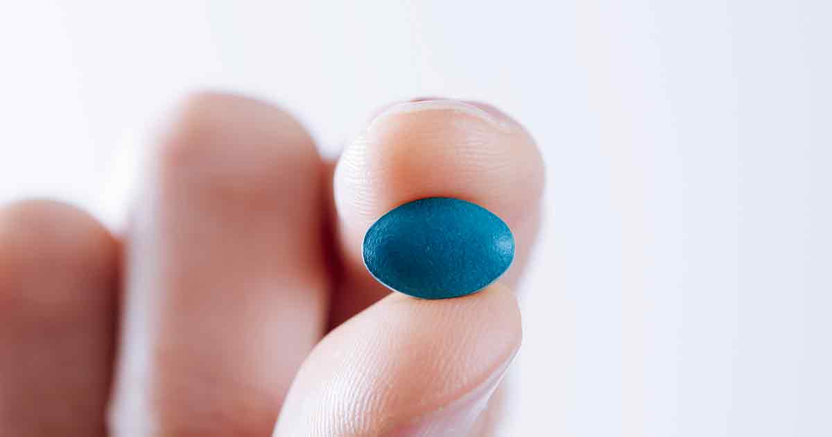 Et nærbilde av en mann som holder en blå pille