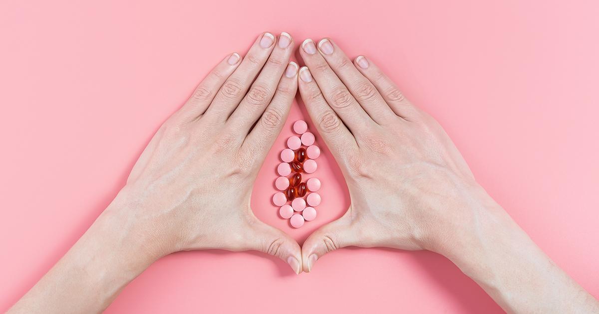 Kobiece dłonie i tabletki układające się w kształt sromu