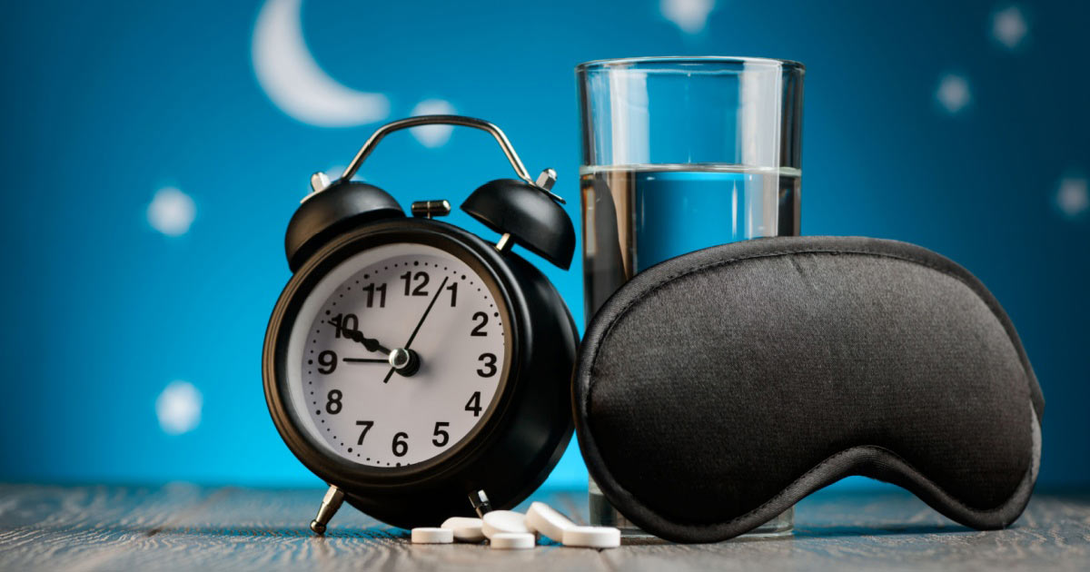 Imagem de relógio, comprimidos, máscara para dormir e copo de água