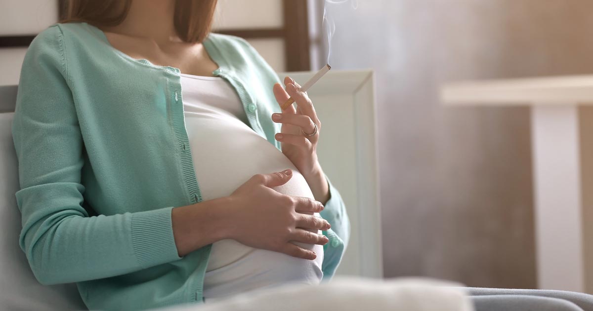 Mulher grávida a fumar um cigarro