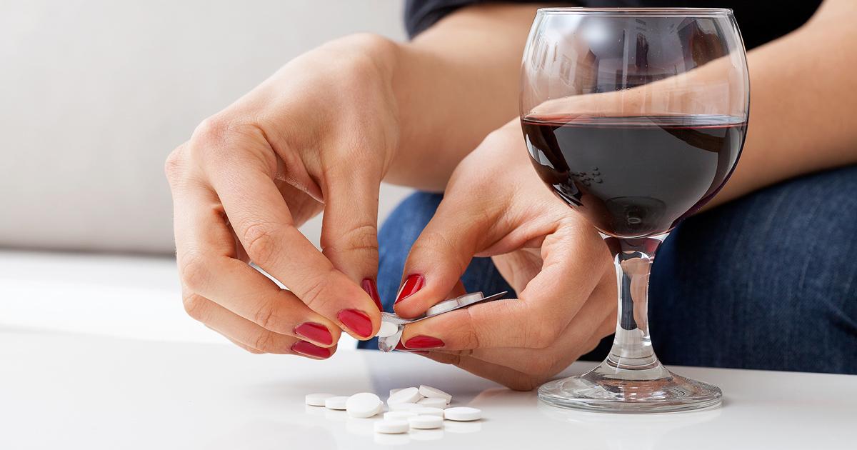uma mulher segurando um copo de vinho e um pacote de comprimidos