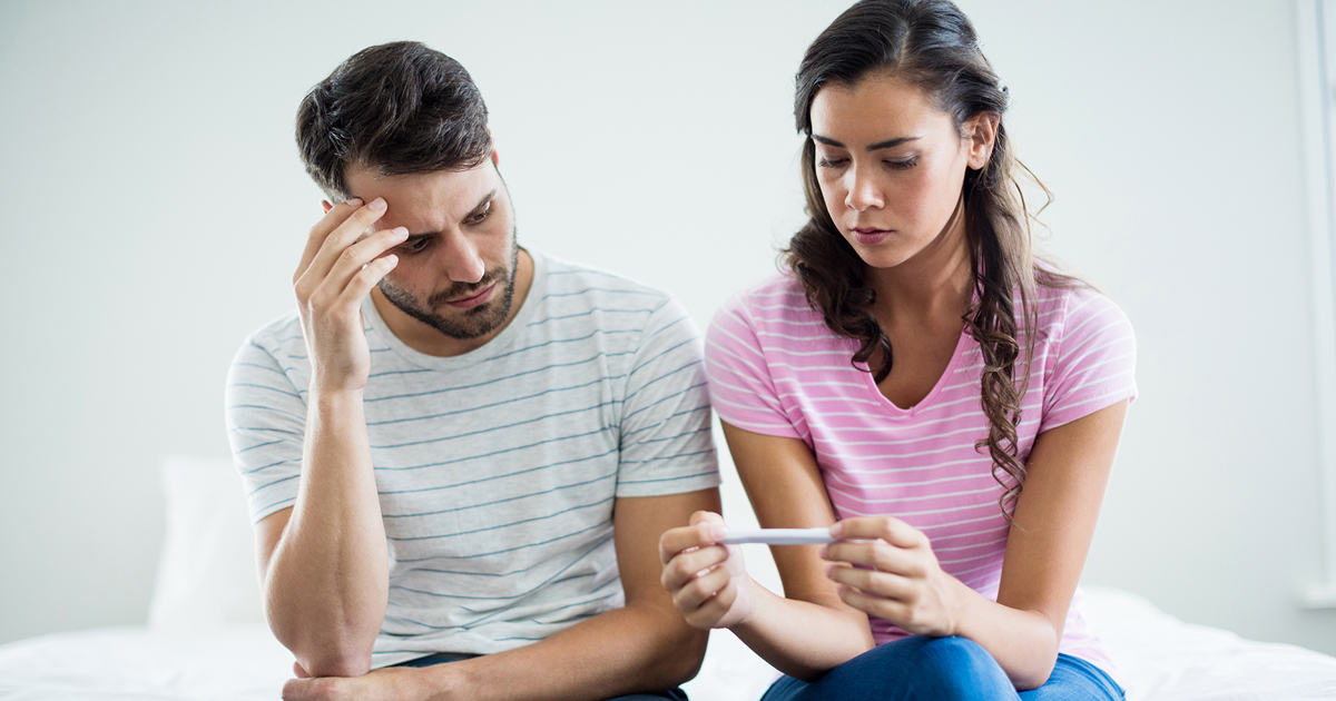 Um casal a olhar desapontado para um teste de gravidez