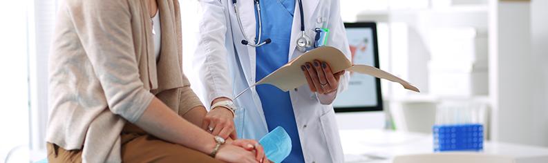 Kvinnlig läkare som lägger en tröstande hand på kvinnlig patient som sitter på en säng