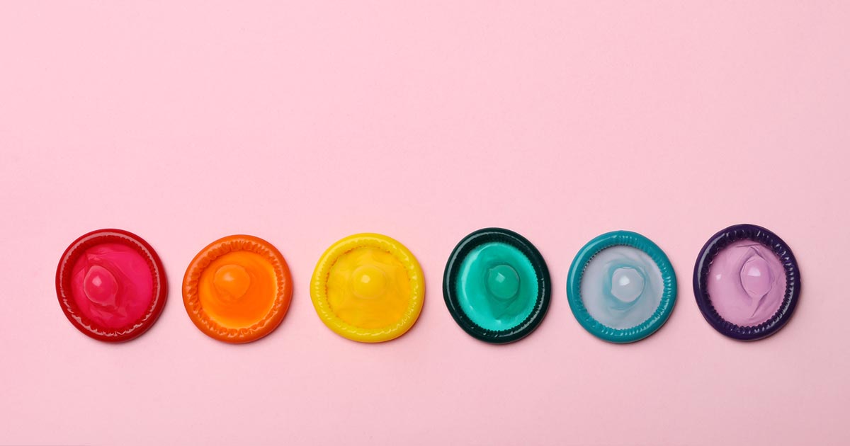 Rad av flerfärgade kondomer på rosa bakgrund.